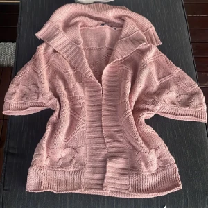 Rosa stickad kofta med kort ärm - Mysig rosa stickad kofta med korta ärmar och bred krage. Koftan har ett snyggt flätmönster och ribbade kanter, perfekt för lager-på-lager. Den är loose fit och passar till chillade dagar eller när du vill vara extra comfy. Endast swish betalning nuläget skickas med spårbart 59kr