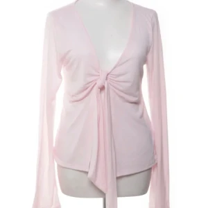 Ljusrosa bolerotopp med knyt framtill - Supersöt ljusrosa bolerotopp från Jinane med lång ärm och djup v-ringning. Toppen har en snygg knyt-detalj framtill som ger en trendig look. Perfekt att styla över ett linne. Mjuk och stretchig i materialet.