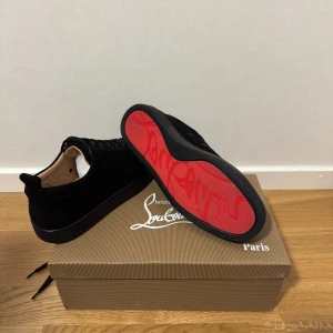 Christian Louboutin svarta sneakers mocka - Snygga svarta sneakers från Christian Louboutin i mocka med klassisk röd sula och svarta snören. Skorna har rund tå och diskreta metalldetaljer på sidan. Perfekta för dig som vill ha en lyxig och stilren look med en ikonisk touch. Jag köpte dem för 1 månad sedan och har använt dem endast en gång. Säljer på grund av att skon är för tajt för min fot.