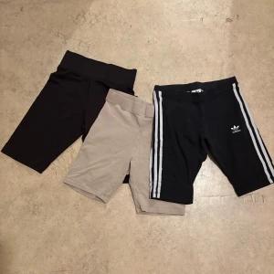 3-pack cykelshorts Adidas & basic - Tre par cykelshorts i olika färger: ett svart par med vita ränder och Adidas-logga, ett beige och ett helsvart. Alla har hög midja och stretchigt material, perfekta för träning eller chill. Adidas-shortsen har klassiska stripes på sidorna.