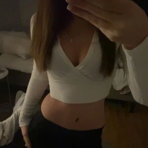 Vit omlottopp från SHEIN XS - Säljer en vit croppad omlottopp från SHEIN i storlek XS. Toppen har långa ärmar, ribbad struktur och djup v-ringning. Materialet är mjukt och stretchigt i polyester och viskos. Perfekt till jeans eller kjol för en trendig look.