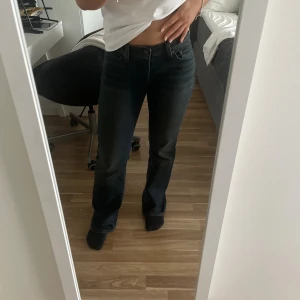 Levi's Superlow Bootcut jeans - Säljer ett par svarta Levi's Superlow Bootcut jeans i klassisk denim. Modellen har låg midja och bootcut-ben, vilket ger en snygg siluett. Jeansen har fem fickor och klassisk Levi's-lapp bak i midjan. Säljer då de är lite för stora för mig. Storlek: W27 L32