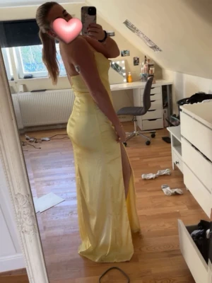 Gul långklänning med slits - Säljer min gamla balklänning! Använd 1 gång. Den är från Nelly och det är en lång maxi dress med smala axelband. Materialet är glansigt och ger en lyxig känsla, perfekt för speciella tillfällen.