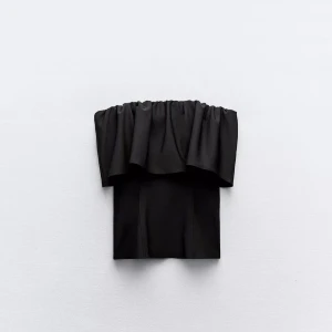 Svart bandeau tubtopp med volang - Säljer en svart bandeau tubtopp med bred volang upptill. Toppen är axelbandslös och har en snygg, flowy look som sitter tight runt bröstet. Perfekt att styla med jeans eller kjol för en trendig vibe.