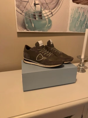 Grå Philippe Model sneakers - Säljer ett par snygga grå sneakers från Philippe Model med vita detaljer och logga på sidan. Skorna har snörning, rund tå och platt sula. Materialet är en mix av mocka och syntet, vilket ger en schysst och modern look. Perfekta för dig som gillar stilrena och bekväma sneakers. Dem är ungefär 1 månads använda bara