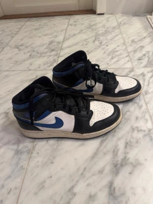 Nike Air Jordan 1 svart/blå/vit - Säljer ett par Nike Air Jordan 1 med svart, blå och vit färgkombination. Skorna är använda, men har fortfarande ett bra skick. Köpta för runt 1800kr