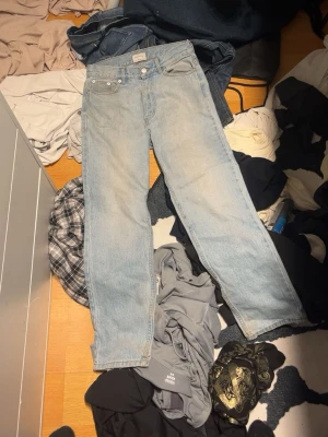 Ljusblå jeans  - Säljer ett par klassiska ljusblå jeans fmed rak passform och femficksdesign. Jeansen har en enkel look med knappgylf och är perfekta för en chill och avslappnad stil. Materialet är slitstarkt jeans i bomull.