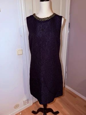 Mörkblå klänning med pärldetaljer STOCKH LM - Säljer en mörkblå, ärmlös kortklänning från STOCKH LM i storlek 40. Klänningen har en strukturerad yta, rund hals med pärldetaljer i guld och dragkedja bak. Materialet känns lyxigt och har en lätt glans. Perfekt för dig som vill sticka ut.