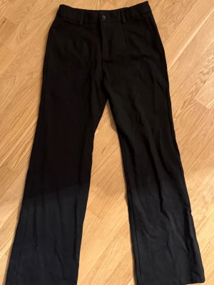 Svarta kostymbyxor Sisters Point XS - Svarta kostymbyxor från Sisters Point i storlek XS. Byxorna har raka ben, bälteshällor och stängs med knapp och dragkedja. Snygg och stilren modell som passar till många olika looks.