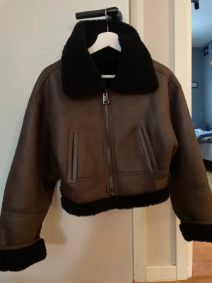 Brun teddyjacka från MNG XS - Säljer en brun teddyjacka från MNG i storlek XS. Jackan har svart fuskpäls på krage, ärmslut och nederkant, samt dragkedja framtill. Croppad modell med två fickor och snygga detaljer i svart. Perfekt för kalla dagar när du vill vara både varm och stilren.