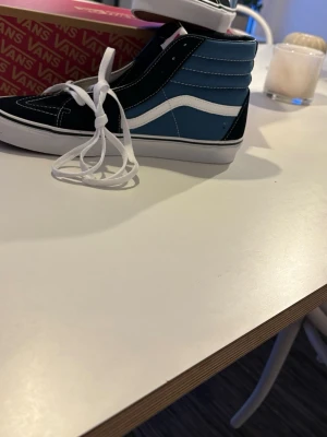 Vans Sk8-Hi blå och svarta sneakers - Säljer ett par Vans Sk8-Hi sneakers i blått och svart med vit sula och klassisk vit sidestripe. Skorna har högt skaft, vita snören och kontrastsömmar. Materialet är en mix av mocka och canvas för en skön streetlook.