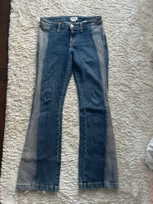 Weekday jeans  - Här är en snygg och naturlig svensk version, anpassad för t.ex. annons eller försäljning:  Blå lågmidjade bootcut-jeans från Weekday i storlek W25. Smickrande passform med utsvängda ben och en cool tvätt med ljusare partier längs benen.  ✔ Stilren vintageinspirerad tvätt ✔ Bootcut / utsvängda ben ✔ Låg midja ✔ Mjuk denim med fin struktur  ⚠ Skicknoteringar: 	•	Lätt slitage baktill vid byxbenens fållar, se bild 4 	•	Varumärkespatchen baktill är sprucken, se bild 5  Båda detaljerna är enbart kosm