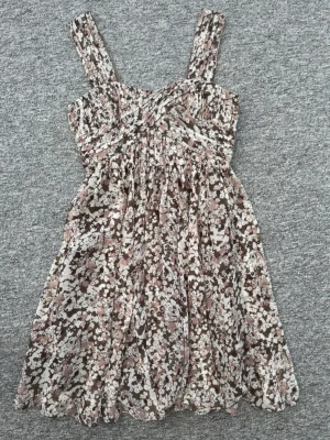 Blommig klänning  - Supersöt kortklänning med breda axelband och blommigt mönster i brunt, vitt och rosa. Helt ny med prislapp kvar, ordinarie pris 799, Klänningen har ett omlottliknande liv. Stl 38