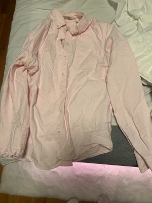 Ljusrosa oxfordskjorta från Gant - Säljer en klassisk ljusrosa oxfordskjorta från Gant i bomull. Skjortan har lång ärm, bröstficka och knappar hela vägen. Perfekt oversized eller normal passform beroende på stil. Enkel att styla till olika looks.