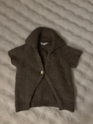 Brun stickad kofta från Zara - Slutsåld Kortärmad brun stickad kofta från Zara med bred krage och en knapp framtill. Perfekt att slänga över en topp under kyligare dagar!