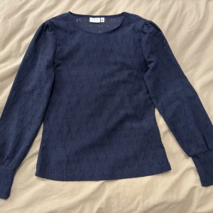 En marinblå tröja från Vila  - Tröjan har dekorativa ihåliga mönster som ger ett elegant uttryck. Den har även resår vid ärmsluten som ger den en extra fin passform på ett stilrent sätt 