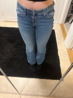 Blå bootcut jeans med låg midja, 170 - Säljer ett par ljusblå jeans med bootcut-modell och låg midja. Jeansen har klassiska fem fickor, gylf med dragkedja och knapp samt snygga detaljer på bakfickorna. Jeansen är i storlek 170 men jag rekomderar de om man är lite under. Perfekta för dig som gillar en retroinspirerad look och vill ha ett par jeans som sitter snyggt över höfterna.