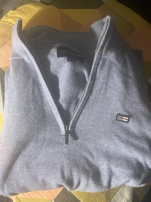 Blå Lexington half zip tröja - Snygg blå tröja från Lexington med half zip och ribbade muddar. Klassisk logga på bröstet och hög krage. Perfekt för dig som gillar stilrena och bekväma plagg. Materialet känns mjukt och passar till både skola och chill.