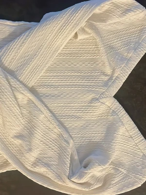 Vit ribbad stickad topp från SHEIN - Säljer en vit ribbad stickad topp från SHEIN i storlek XS. Toppen har ett omlott-snitt och långa ärmar med breda muddar. Materialet är mjukt och stretchigt med ett snyggt kabelstickat mönster som ger en trendig look.