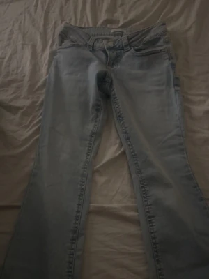 Ljusblå bootcut jeans med fickdetaljer - Säljer ett par ljusblå jeans med bootcut passform och snygga fickor med lock och knapp bak.