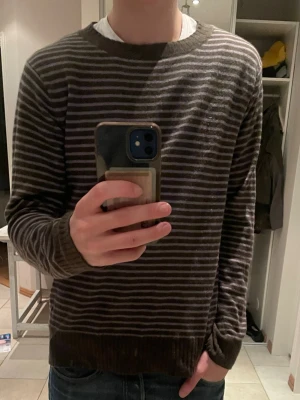 Kaschmir blend tröja från Henry Choice - Säljer en mörk grön långärmad tröja från Henry Choice med tunna horisontella ränder i ljusgrått. Tröjan har rund halsringning och ribbade muddar vid ärmslut och nederkant. Perfekt för dig som gillar en enkel men stilren look.