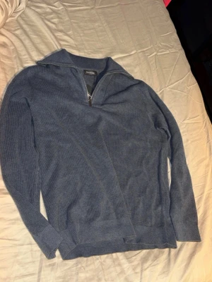 Blå stickad half zip tröja Dressmann - Säljer en marinblå stickad tröja från Dressmann med half zip-dragkedja och hög krage. Tröjan är ribbad och har lång ärm, perfekt för kyligare dagar. Enkel och stilren design som passar till det mesta.