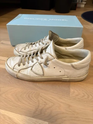 Vita Philippe Model sneakers i skinn - Säljer ett par vita Philippe Model sneakers i skinn med klassisk låg profil och rund tå. Skorna har snörning och diskret logga på sidan. Perfekta för dig som gillar stilrena och tidlösa sneakers med exklusiv känsla.