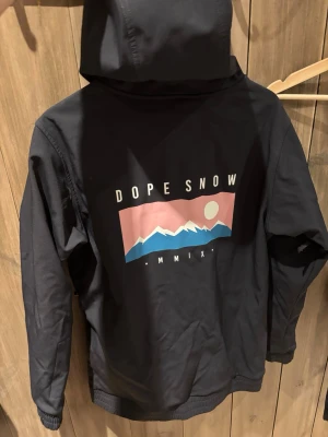 Svart vindjacka från Dope Snow - Svart vindjacka med huva från Dope Snow. Jackan har vita snören i huvan, dragkedjeförsedda fickor och ribbade muddar. Nypris runt 2000kr!