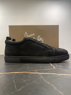 Svarta mocka sneakers från Louboutin - Säljer ett par svarta sneakers från Christian Louboutin i mjuk mocka med rund tå och platt sula. Skorna har svarta snören och diskreta sömdetaljer för en clean look. Perfekta för dig som gillar stilrena och exklusiva sneakers.