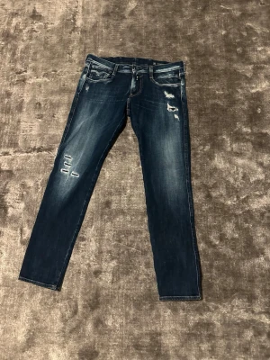 Replay Anbass - Säljer ett par Replay Anbass jeans i mörkblå tvätt med slitningar och skinny/slim passform. Klassiska femficksjeans med snygga detaljer på bakfickorna och normal passform i midjan. Tillverkade i stretchig jeansbomull för skön känsla. De är små i storleken.