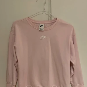 Ljusrosa sweatshirt från Nike - Säljer en ljusrosa sweatshirt från Nike med broderad logga framtill. Tröjan har rund halsringning och långa ärmar. Tillverkad i mjuk bomullsblandning, perfekt för chill dagar eller till träningen. Den är endast använd fåtal gånger och är som ny!! Jag skulle säga att den är i storlek 146-152. 