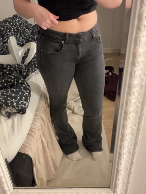 Svarta bootcut jeans från lager 157 - Säljer ett par grå/svarta bootcut jeans från lager 157 med klassisk femficksdesign och dragkedja. Jeansen har en snygg mörkgrå tvätt och är tillverkade i ett mjukt jeansmaterial som sitter skönt på kroppen. Perfekta för dig som gillar en avslappnad men ändå trendig look.