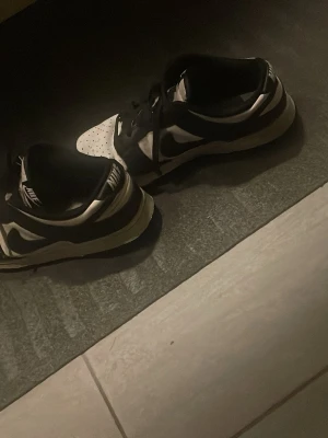 Nike Dunk Low svart/vit sneakers - Säljer ett par Nike Dunk Low sneakers i svart och vitt. Skorna har klassisk låg siluett, svart swoosh och snörning framtill. Ovandelen är i skinn med perforerad tåbox för extra ventilation. Perfekta för dig som gillar streetstyle och vill ha en ikonisk look. Lite smutsiga men går att tvätta bort själv. Använda i cirka några månader men inga problem med dom!