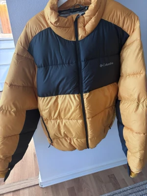  pufferjacka Columbia XL - Säljer en riktigt fet pufferjacka från Columbia Black&Yellow limited edition, i storlek XL. Jackan är gul med svarta partier, har dragkedja framtill och är perfekt för kalla dagar. Oversized vibe och riktigt skön att bära. Materialet är syntet 
