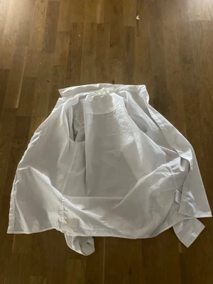 Vit skjorta från H&M i bomull - Klassisk vit skjorta från H&M i bomull. Skjortan har lång ärm, knappar hela vägen framtill och en enkel, stilren krage. Perfekt till jeans eller chinos för en clean look.