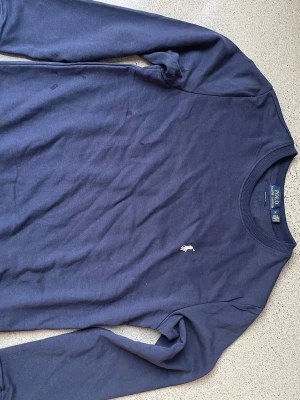 Mörkblå långärmad tröja Polo Ralph Lauren - Säljer en mörkblå långärmad tröja från Polo Ralph Lauren i bomull. Klassisk rund halsringning och broderad logga på bröstet. Custom fit-modell som sitter snyggt och passar till många olika stilar.