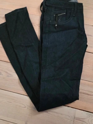 G-Star Raw Skinny Jeans Svart 27/34 - Säljer ett par svarta skinny jeans från G-Star Raw, modell New Ocean Skinny WMN. Jeansen har dragkedjor på bakfickorna och är tillverkade i ett klassiskt jeansmaterial. Snygg och modern passform som sitter tight hela vägen.