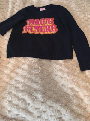 Svart Kashmir tröja From Future - Cool mörkblå Kashmir tröja från From Future med färgglad text 'MAGIC FUTURE' i rosa, gul och orange på bröstet. Tröjan har rund halsringning och långa ärmar. Perfekt för dig som vill sticka ut med en unik statement piece.