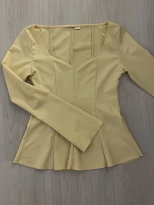 Gina Tricot - Supersnygg ljusgul blus från Gina young 14+ med v-ringad hals och figurnära passform som markerar midjan. Blusen har långa ärmar och en lätt utsvängd nederdel. Storlek S❣️