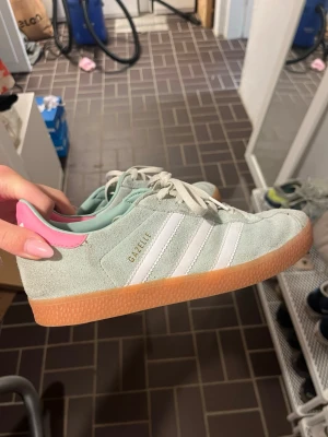Adidas Gazelle mintgrön/rosa sneakers - Säljer ett par Adidas Gazelle sneakers i mintgrönt mocka med vita ränder och snörning. Använda fåtal gånger. Köpts på nk i Göteborg 