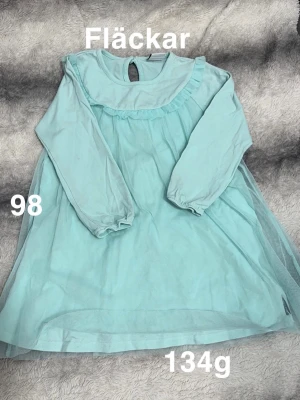 Ljusblå långärmad klänning stl 98 - Söt ljusblå klänning med långa ärmar och volangdetalj vid halsen. Klänningen har ett tunt lager tyll över kjolen och en knapp i nacken för enkel påklädning. Perfekt för dig som gillar en romantisk look.🌸 Fläckar. Storlek 98