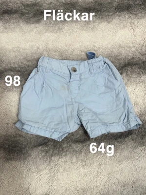 Ljusblåa shorts med knapp - Ljusblåa shorts med klassisk passform och knapp framtill. Shortsen har två sidofickor och resår i midjan för extra komfort. perfekta för varma dagar.🌸 Fläckar. Storlek 98