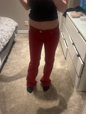 Röda bootcut byxor med dragkedjor - Snygga röda byxor med bootcut passform och coola dragkedjor på bakfickorna. Byxorna har låg midja och sitter riktigt bra över höfterna.  Materialet känns mjukt och följsamt.