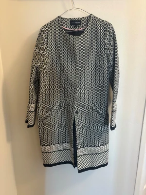 Svartvit mönstrad rock från KappAhl - Säljer en svartvit rock från KappAhl med grafiskt rutigt mönster och kontrasterande kantmönster nertill och vid ärmslut. Jackan är långärmad, har rund halsringning och knäpps med knappar framtill. Perfekt för dig som gillar statement-plagg!