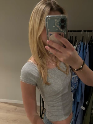 Grå ribbad topp med spetskant 157 - Superfin ljusgrå ribbad topp från 157 i storlek S. Toppen har korta ärmar och är dekorerad med söt spetskant längs halsringningen och ärmsluten. Perfekt att styla med jeans eller kjol för en chill look.