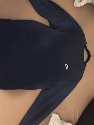 Mörkblå Nike sweatshirt - Säljer en Helt ny oanvänd mörkblå sweatshirt från Nike med klassisk vit logga på bröstet. Tröjan har rund halsringning och långa ärmar, perfekt för en chill och sportig stil. Materialet är mjukt och skönt, troligtvis bomull eller polyester. Passar dig som gillar enkel och stilren design.