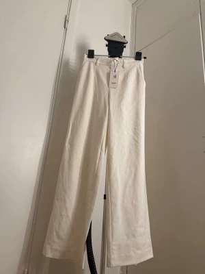 Vita wide byxor från OBJECT - Säljer ett par snygga vita byxor från OBJECT med breda ben och hög midja. Byxorna har resår i midjan bak, bälteshällor och diskreta bakfickor. Tillverkade i ett mjukt bomullsmaterial som känns fräscht och stilrent.