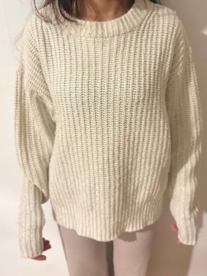 Beige stickad oversized tröja - Säljer en chunky beige stickad tröja med oversized passform och långa ärmar. Tröjan har grov ribbstickning och en högre rund halsringning. Perfekt för lager-på-lager och chill dagar.