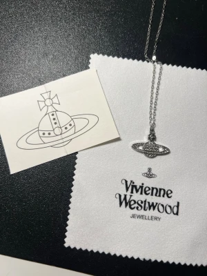 Silvrigt halsband Vivienne Westwood - Säljer ett ikoniskt halsband från Vivienne Westwood i silverfärg. Kedjan är tunn och smidig, och hänget har det klassiska orb-motivet med små gnistrande stenar. Kommer med originalpåse och ask. Perfekt accessoar för dig som vill sticka ut.