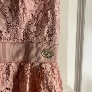 Rosa spetsig linnetopp från Chiara Forti - Supersöt ljusrosa linnetopp från Chiara Forti med tunna justerbara axelband, spetsdetaljer och volang nedtill. Toppen har en bred midjerem med metallmärke!